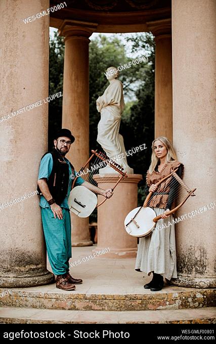 Male and female couple holding lyra musical instrument by pillar