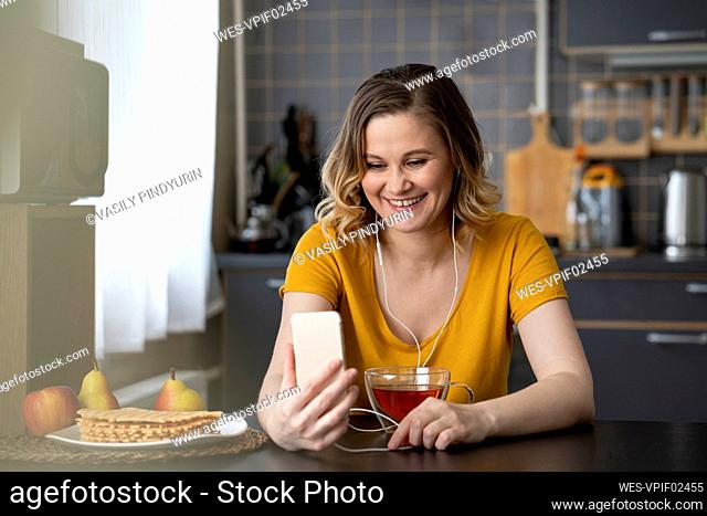 Happy woman having a video chat with smartphone in kitchen at home