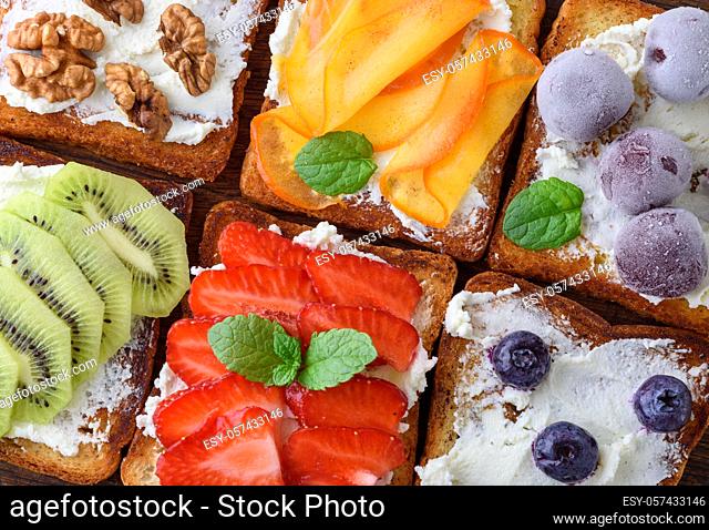 French toasts with soft cheese, strawberries, kiwi, walnuts, cherries and blueberries on a brown wooden board