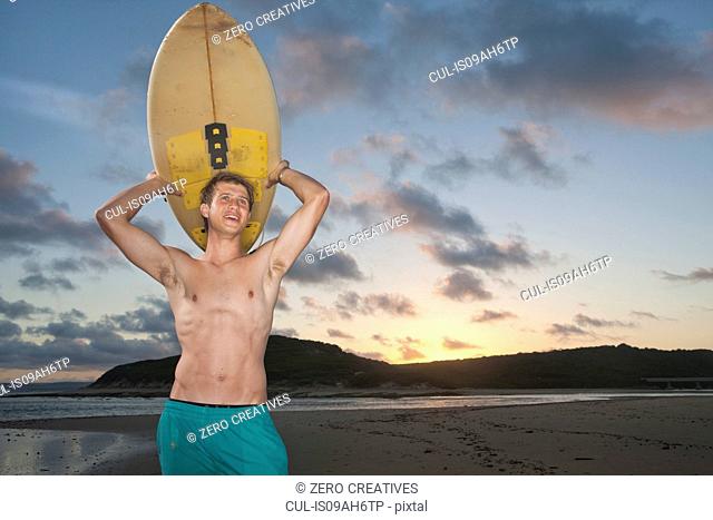 Surfer standing on beach carrying surfboard