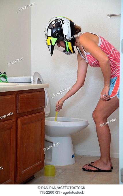 A woman wearing a helmet cleaning a toilet