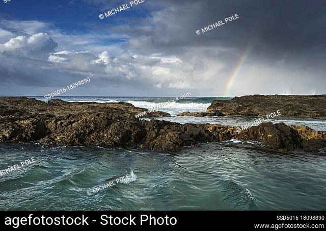 Rainbow in stormy skies and waves crashing onto rocky coast