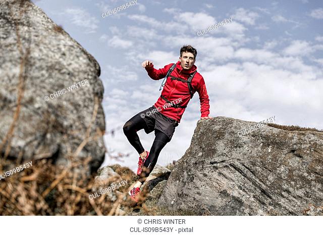 Male runner running between boulders on Stanage Edge, Peak District, Derbyshire, UK