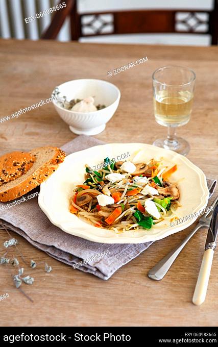 Mixed vegetable stir fry with mushrooms and cottage cream cheese. Tender mushroom stir fry served in a white plate with white wine and bread on the wooden table