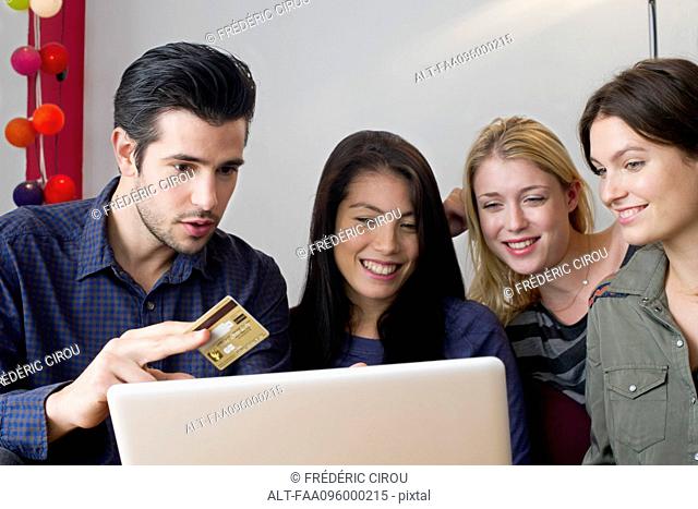 Friends gathered around laptop computer preparing to use credit card for online purchase