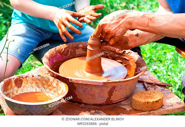 Teacher helps his student to work with red clay. Work on the potter's wheel at the outdoors