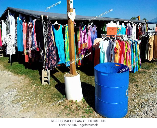 A blue barrel, signpost and hanging clothes in a vendor's booth at an intersection of paths at a weekly flea market in rural Ontario, Canada