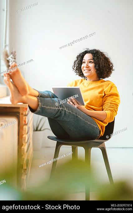 Happy beautiful woman sitting with tablet PC on chair at home