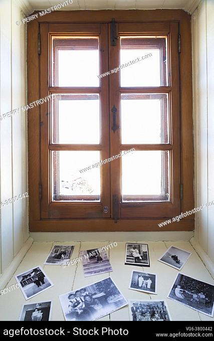Black and white family photographs on white painted wood plank windowsil in office room on upstairs floor inside an old 1807 cottage style house, Quebec, Canada