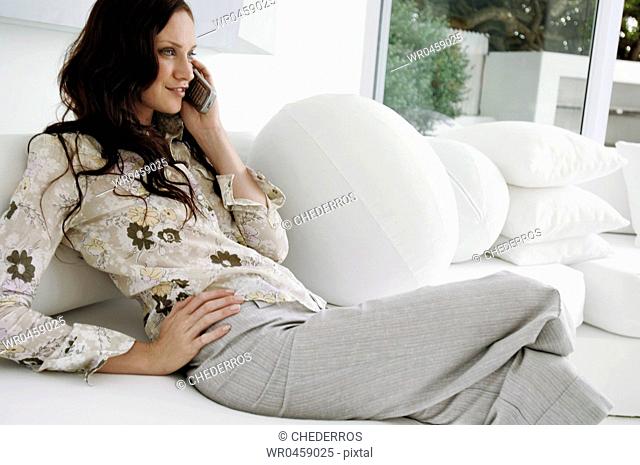 Mid adult woman sitting on a couch and talking on a mobile phone