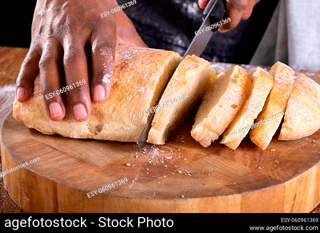 Close-up of african american male baker slicing bread on wooden cutting board