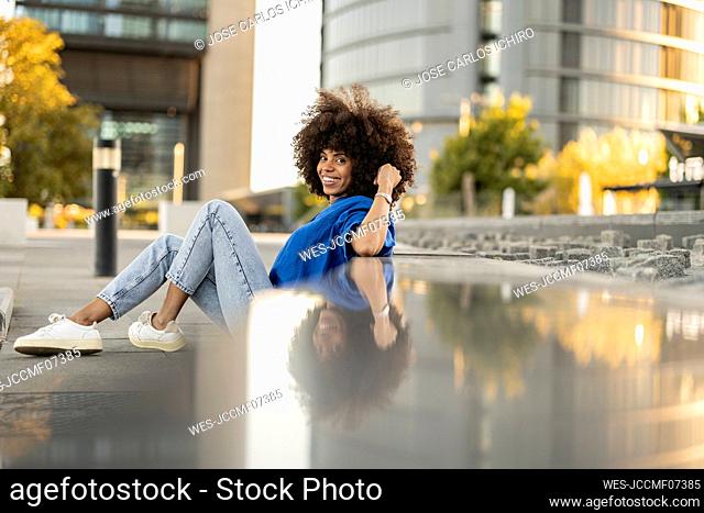 Smiling woman with Afro hairstyle leaning on wall
