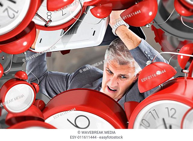 Composite image of angry businessman breaking laptop