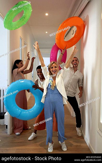 Playful male and female colleagues playing with inflatable rings at corridor
