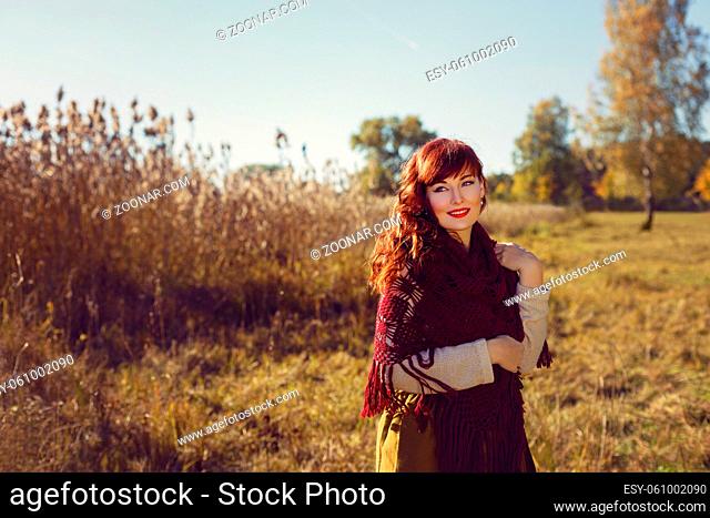 Beautiful young woman in long skirt and red wool scarf standing outdoors in countryside. Outdoor shot. Natural background. Copy space