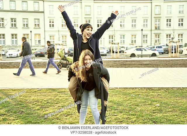 lively woman carrying best friend piggy back, cheerful, arms raised, in city Cottbus, Brandenburg, Germany