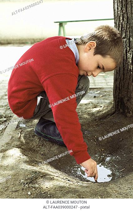 Boy crouching, playing in puddle, side view