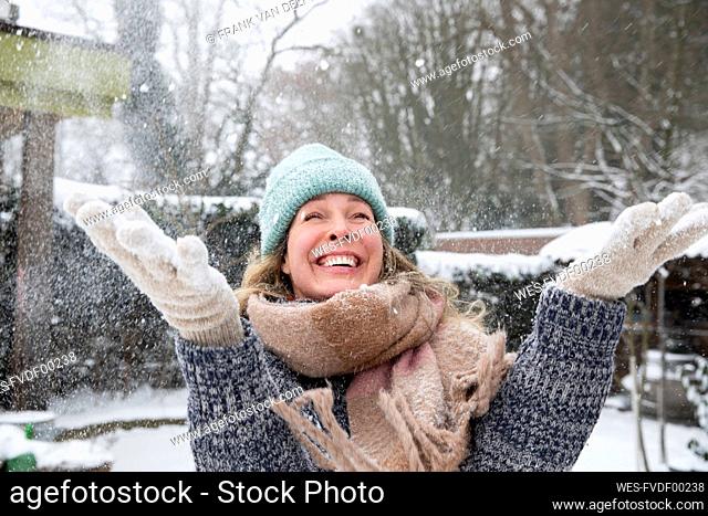 Playful mature woman throwing snow at backyard during winter