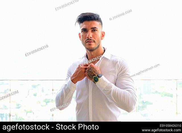 Portrait of young handsome Persian businessman with beard stubble against view of the city