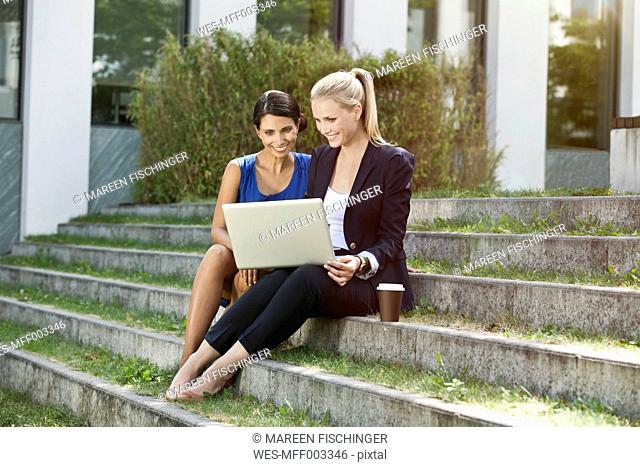 Two businesswomen sitting on stairs outside using a laptop