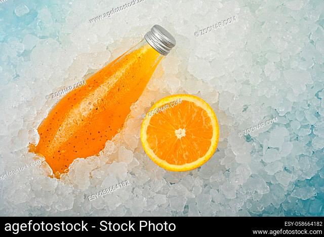 Close up one glass bottle of cold orange juice cocktail drink with chia seeds and half cut orange on crushed ice at retail display, elevated high angle view