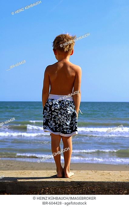 Boy on the beach looking out of the sea, Caorle, Veneto, Italy