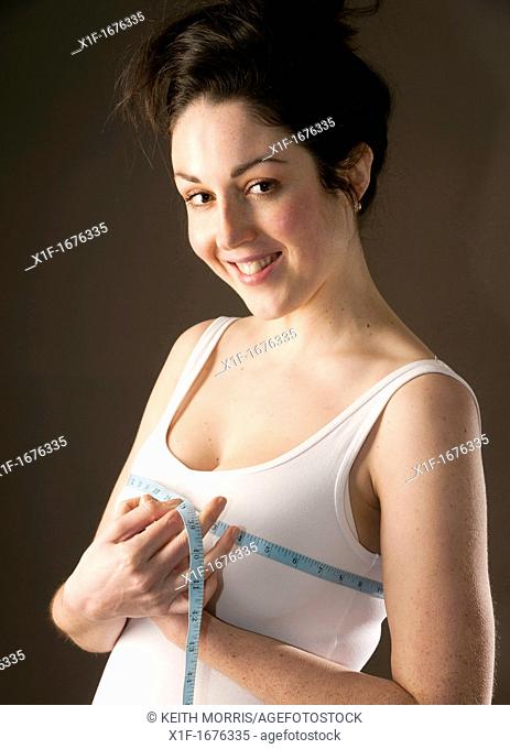 A young woman with brown hair and eyes measuring her body checking the size of her breasts chest tits bosom
