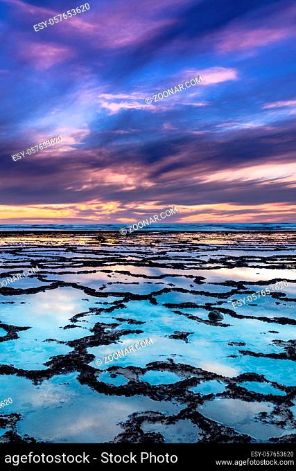 A vertical view of a beautiful sunset over the ocean with rocky beach and tidal pools in the foreground