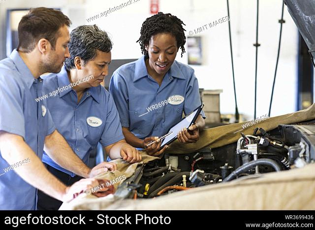 Three mechanics sharing a digital tablet and planning work on a car in for repair