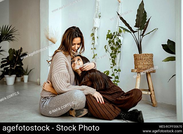 Smiling mother and daughter looking at each other while sitting on floor at home