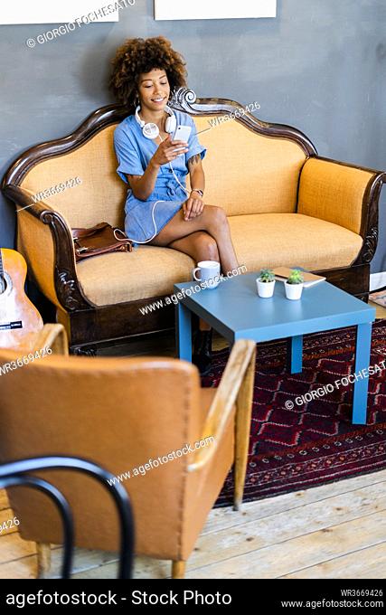 Young woman using smart phone while sitting on sofa in modern cafe