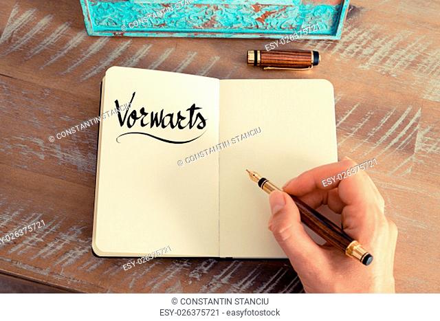 Retro effect and toned image of woman hand writing a note on a notebook. Handwritten text in German &quot;Vorwarts&quot; - translation