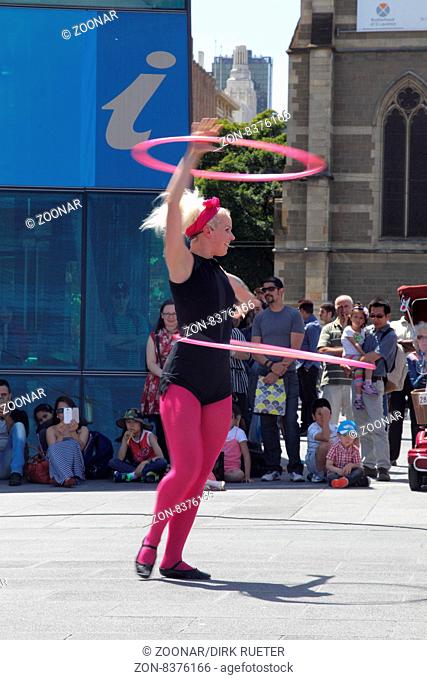 Akrobatin zeigt eine Hula-Hoop Performance auf dem Federation Square in Melbourne, Victoria, Australien. Street performer showing a hula-hoop performance on...