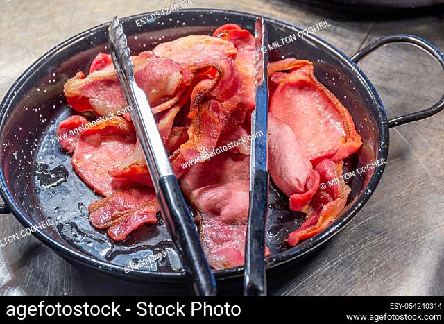 Pile of cooked back bacon in a serving skillet with tongs