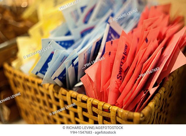 Packets of Sweet N' Low, Equal, and Splenda and raw sugar on a counter in a cafe