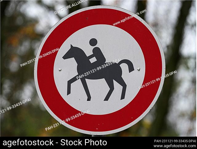PRODUCTION - 21 November 2023, Brandenburg, Stahnsdorf: The depiction of a rider and horse on a white sign with a red border at the start of a forest path means...