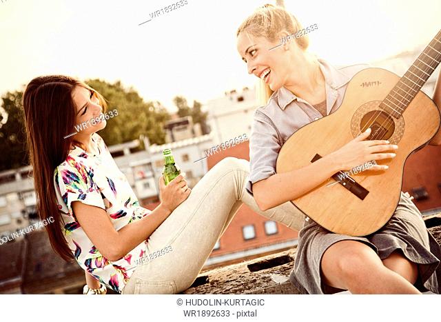 Young woman with girlfriend playing guitar at rooftop party