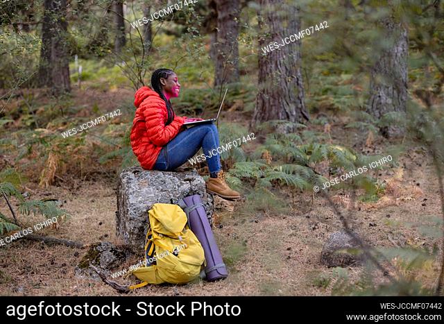 Happy woman using laptop sitting on rock in forest