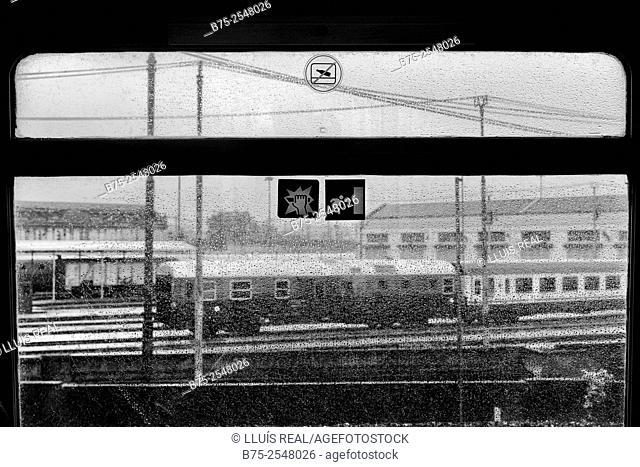 View from the window of a train on a rainy day of the platforms of a train station of Milan, with rail tracks, poles with electrical wires and two vagons