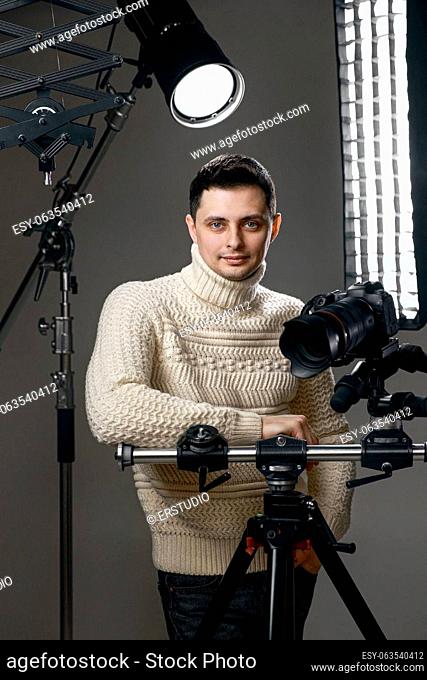 Professional handsome photographer with digital camera on tripod on gray background with lighting equipment