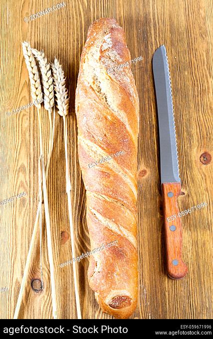 one fresh light-colored bread with a delicious crisp, close-up in the kitchen with a knife and spikelets of stump