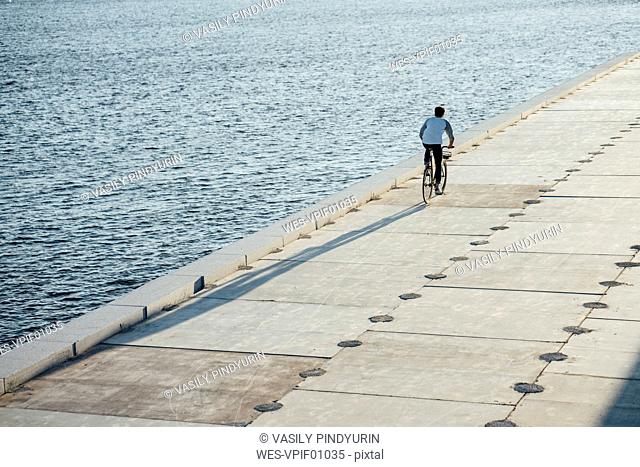 Young man riding bike on waterfront promenade at the riverside