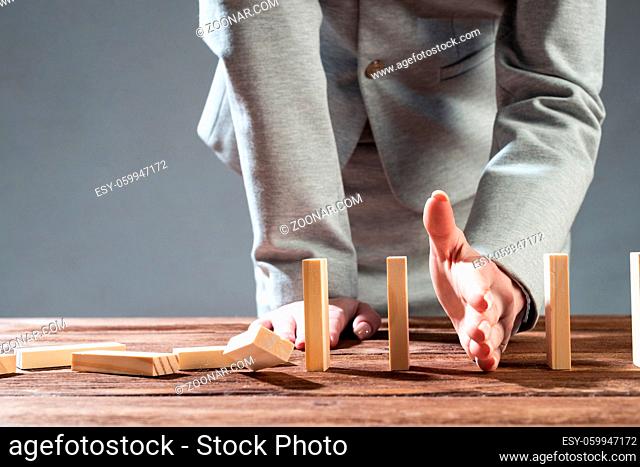 Businesswoman protecting dominoes from falling on wooden desk. Business assistance and leadership in crisis. Operative business solution and stabilization of...