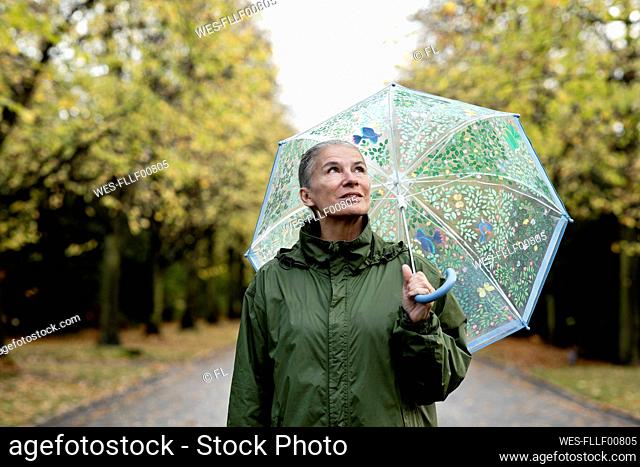 Contemplative senior woman with raincoat and umbrella
