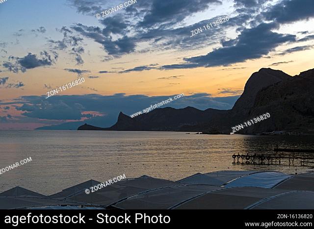 Silhouettes of coastal mountains against the backdrop of the evening sky. View from the embankment of Sudak in the direction of the New World
