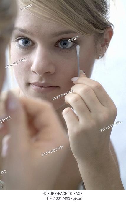 Woman in front of mirror using cotton swab, close-up