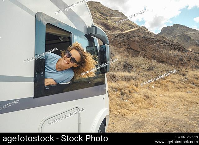 Happy and free single woman smiling and enjoying destination outside the window of her camper van. Concept of renting rv motor home vehicle to travel in holiday...