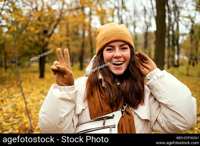 Beautiful woman doing peace sign while standing in autumn park