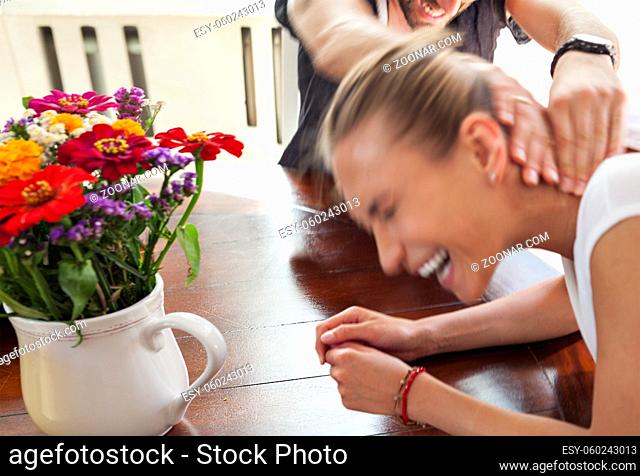 Motion blurred figures of playful young couple indoors. The man is squeezing the woman s neck. Female is laughing