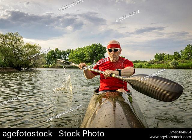 senior male paddler is paddling a long, narrow and fast racing sea kayak on a calm lake, summer scenery in Colorado, POV from an action camera - outdoor fitness...